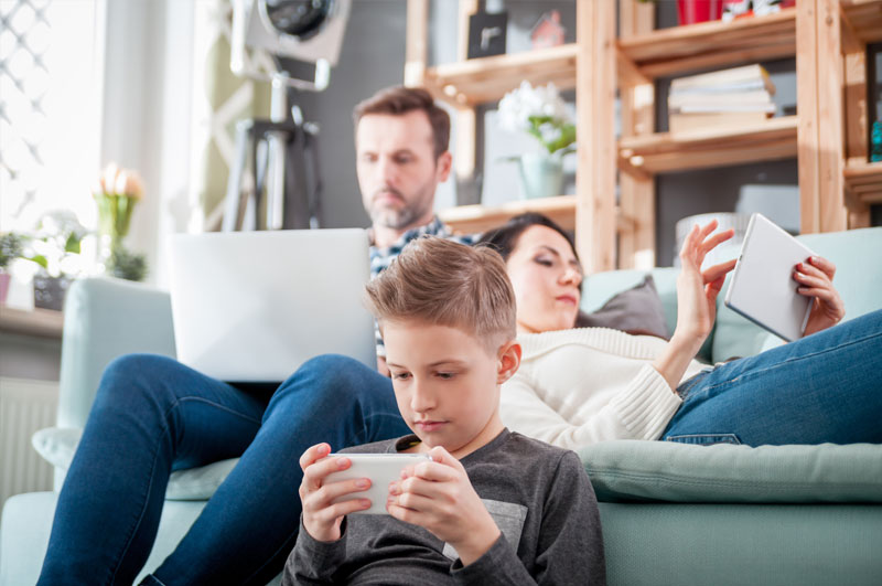 Familie nutzt gemeinsam digitale Geräte wie Smartphone, Tablet und Laptop im Wohnzimmer.